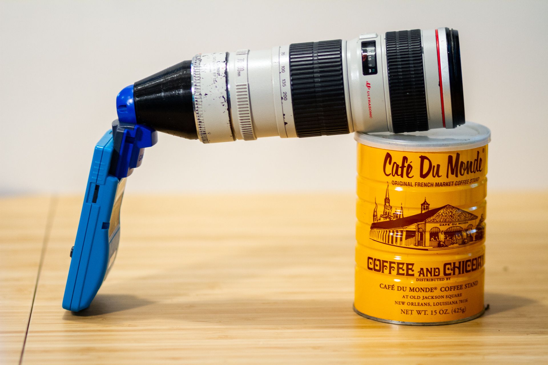A Canon telephoto lens mounted on a Game Boy Camera, resting on a coffee can